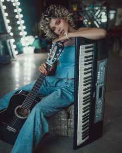 trendy young female musician with guitar and synthesizer resting behind scene money making music