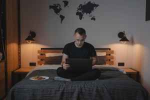 a man using a laptop while sitting on a bed.Digital Nomad Meaning