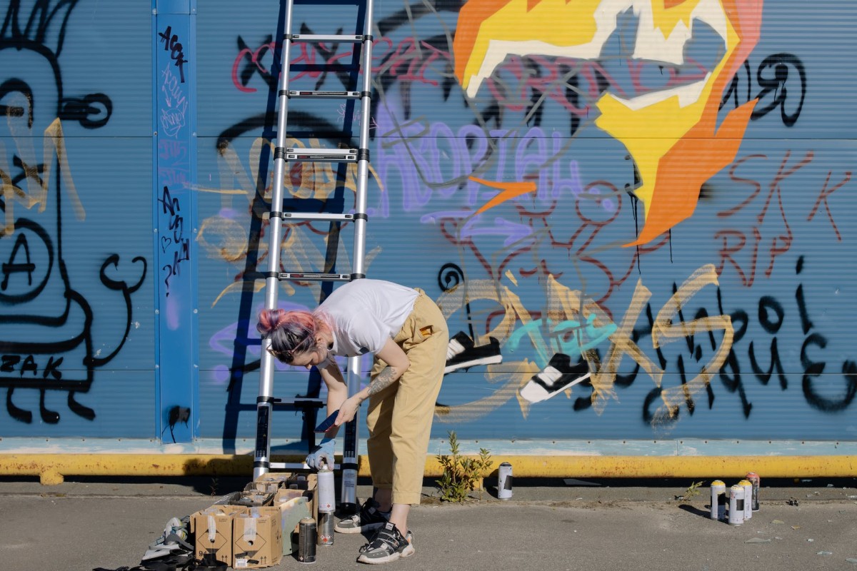 young woman choosing spray paints near graffiti wall on street